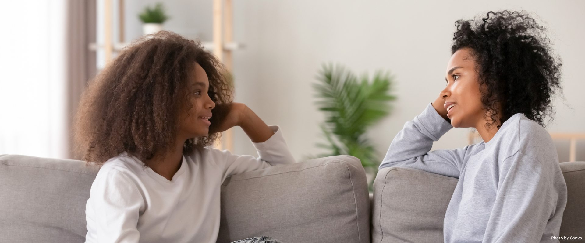 African young mom talk to teen daughter while sitting on couch together