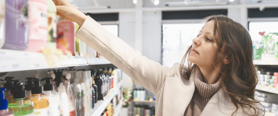 Woman reaching for skincare product on store shelf, choosing body lotion