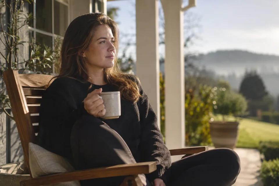 female sitting outside on a porch in early morning, coffee in hand